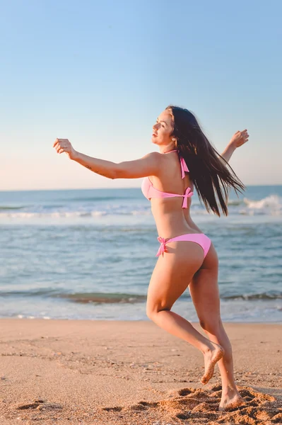 Linda chica en bikini rosa bailando en la playa soleada junto al mar — Foto de Stock