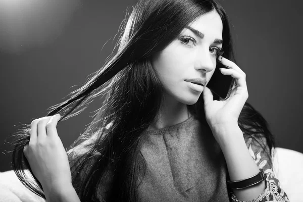 Fotografía en blanco y negro de una hermosa joven hablando por teléfono móvil y mirando sensualmente a la cámara mientras toca el cabello de lujo en el fondo del espacio de copia — Foto de Stock