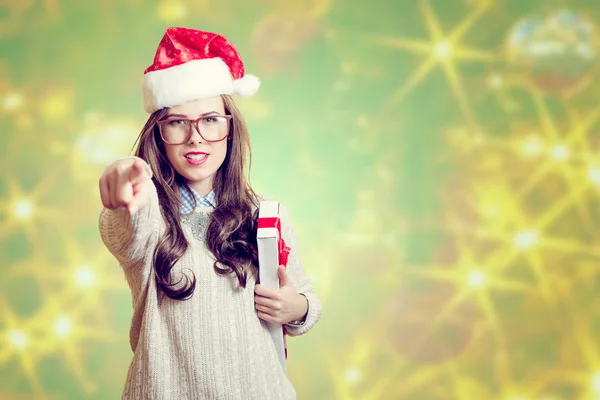 Picture of beautiful young lady in Santa Claus hat on abstract festive background design pointing finger and holding present box — Zdjęcie stockowe