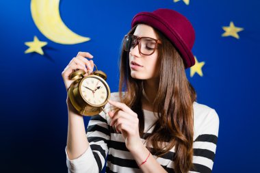 Pretty girl holding alarm-clock on paper stars and moon background