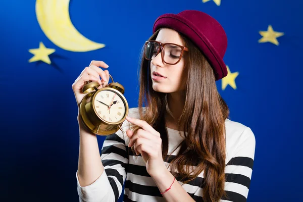 Pretty girl holding alarm-clock on paper stars and moon background — Stock Fotó