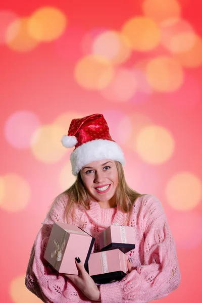 Beautiful lady in Santa hat holding gift boxes with bokeh — Stok fotoğraf