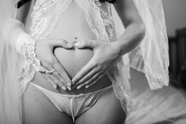 Picture closeup on bridal hands holding love heart sign on pregnant bare belly. Black and white photography — Stok fotoğraf