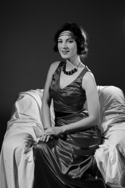 Black and white photography of beautiful young lady in dress relaxing sitting in chair happy smile
