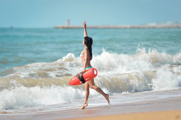 Fit lady in bikini with life-saver running into stormy ocean — Zdjęcie stockowe