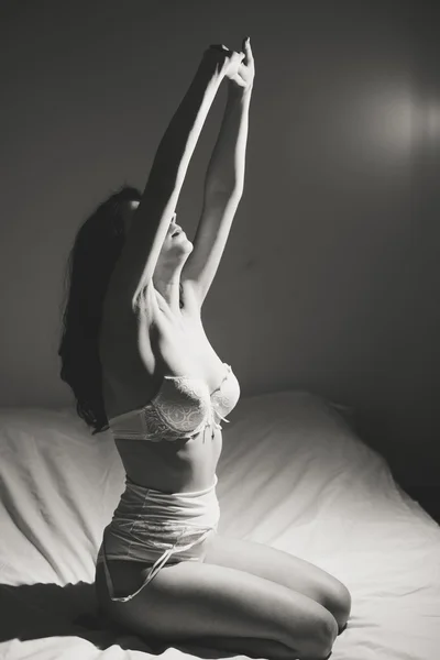 Sexy woman in lingerie sitting on bed stretching hands up — Zdjęcie stockowe