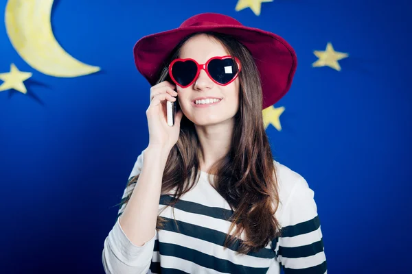 Smiling girl in red hat and sunglasses talking on phone — Stock Photo, Image