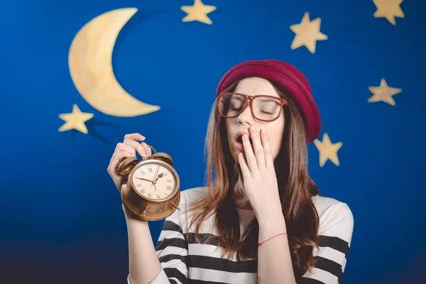 Sleepy yawning beautiful girl holding clocks on night studio background — Stok fotoğraf