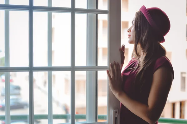 Lovely young brunette in red hat standing in balcony doorway