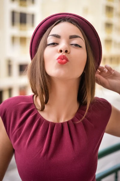 Verspielte Dame mit dunkelrotem Hut und Kleid schickt Kuss — Stockfoto