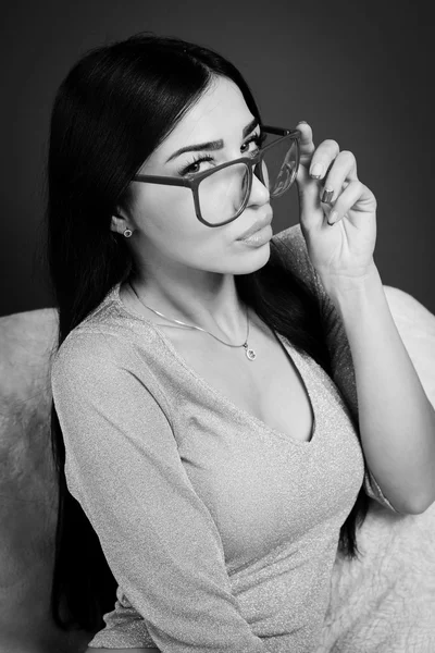 Portrait de jeune jolie dame en lunettes relaxant assis sur une chaise et flirtant en regardant la caméra. Photographie noir et blanc — Photo