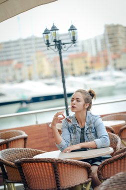 Beautiful young lady holding sunglasses and sitting in street cafe