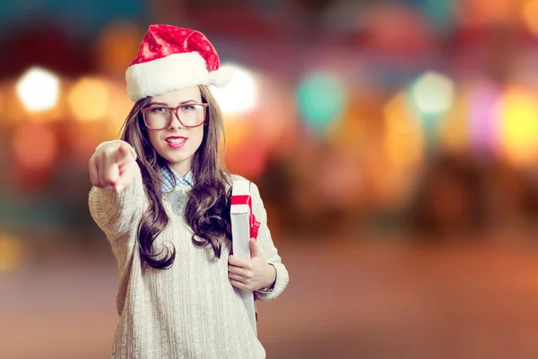 Imagem da bela jovem senhora em chapéu de Papai Noel em abstrato design de fundo festivo apontando dedo e segurando caixa presente — Fotografia de Stock