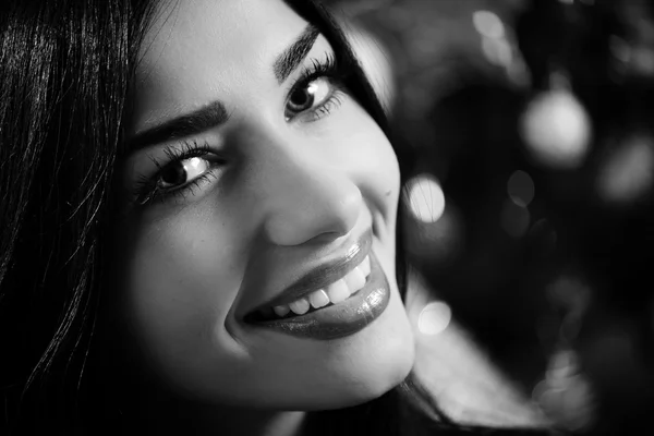 Picture closeup of young beautiful woman happy smiling and looking at camera on Christmas tree background. Black and white image — Stockfoto