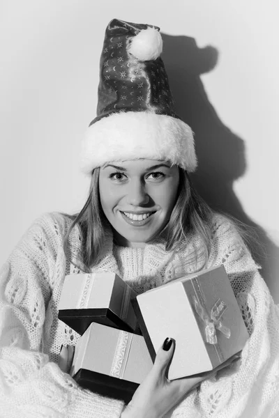 Imagem de feliz sorrindo jovem bela senhora em Santa chapéu segurando caixas de presentes no fundo espaço cópia de luz. Fotografia em preto e branco — Fotografia de Stock