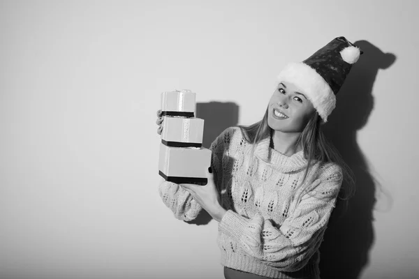 Picture of happy smiling young beautiful lady in Santa hat holding gifts boxes on light copy space background. Black and white photography — Stockfoto