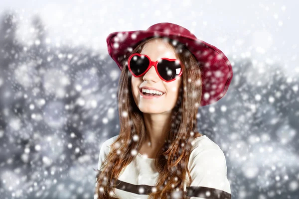 Jovem encantada em chapéu vermelho e óculos de sol desfrutando de queda de neve — Fotografia de Stock