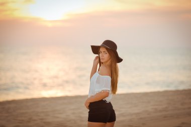 Attractive lady wearing elegant brimmed hat standing on summer beach