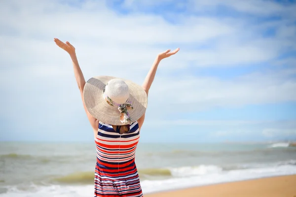 Elegante Frau mit Hut, die die Hände nach oben streckt und sich am Meer ausruht — Stockfoto