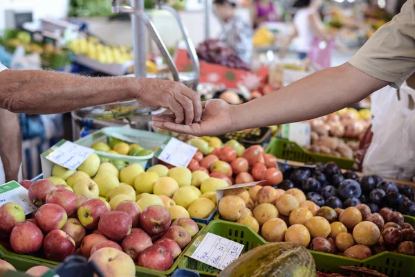 Venditore dando il cambiamento al compratore allo sfondo del banco di frutta fresca — Foto Stock