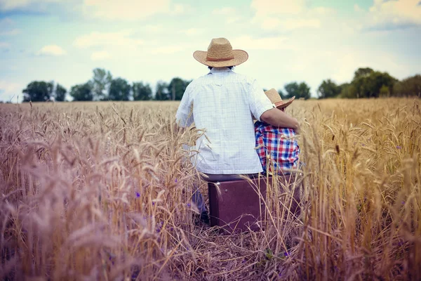 Backview of happy family sitting on old suitcase in farm field — 图库照片
