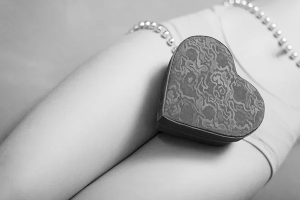 Closeup on present gift box in the form of heart lying on beautiful sexy female legs — Stock Photo, Image