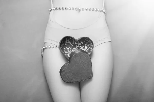 Primer plano en la caja de regalo de regalo abierta en forma de corazón acostado en hermosas piernas femeninas sexy. Fotografía en blanco y negro —  Fotos de Stock