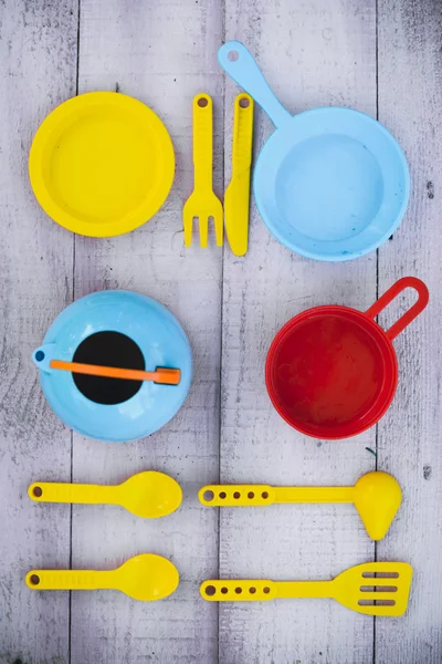 Many colorful plastic toy dishware on lilac wood plank tabletop — Stockfoto