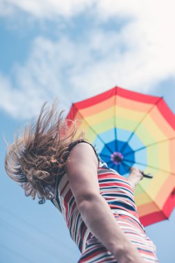 Pretty girl in dress holding rainbow umbrella on sky background