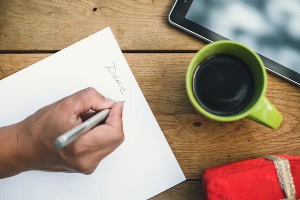 Male hand writing letter beside red giftbox and coffee cup — Stockfoto