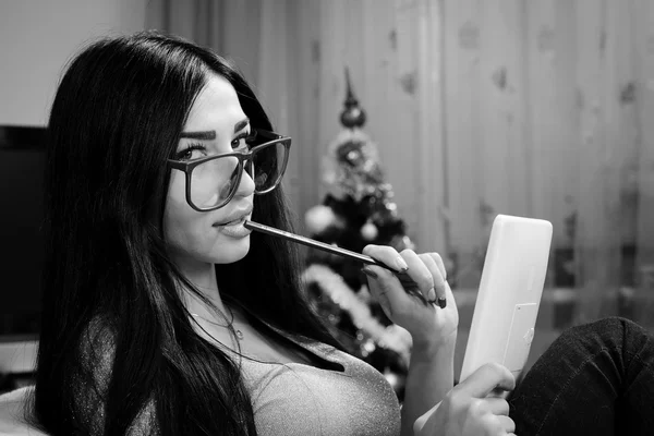 Foto de chica bonita sexy en gafas sosteniendo un ordenador tablet PC relajante sentado en la silla y coqueta mirando a la cámara — Foto de Stock