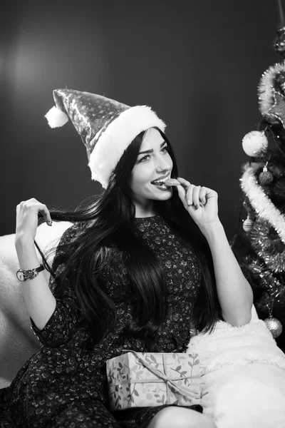 Preto e branco foto de bonita menina no santa claus chapéu segurando caixa de presente e comer fatia de laranja — Fotografia de Stock