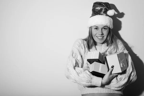 Schwarz-Weiß-Fotografie einer glücklich lächelnden jungen schönen Dame mit Weihnachtsmann-Hut, die Geschenkboxen auf hellem Kopierraum-Hintergrund hält — Stockfoto