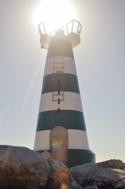 Beautiful lighthouse with bright sun on top on sky background