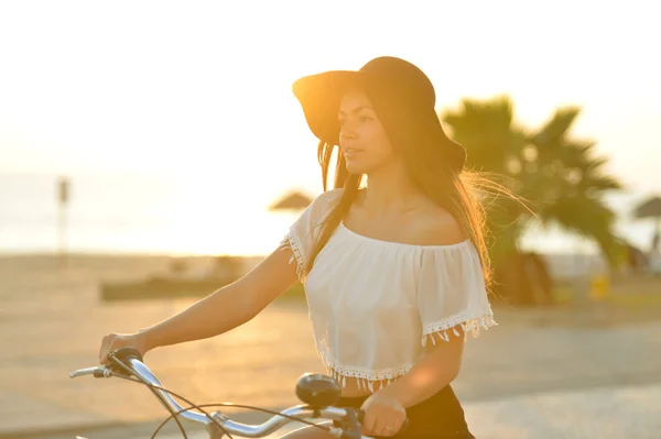 Excited brunette in black floppy hat holding handlebar riding bicycle — Stock Photo, Image