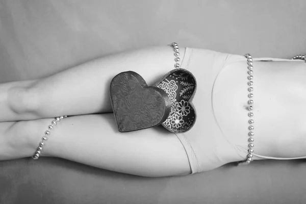 Close-up na caixa de presente aberta na forma de coração deitado em belas pernas femininas sexy. Fotografia em preto e branco — Fotografia de Stock