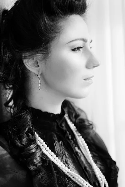 Black and white photography of young beautiful woman standing in the palace room and looking out the window — Stock Fotó