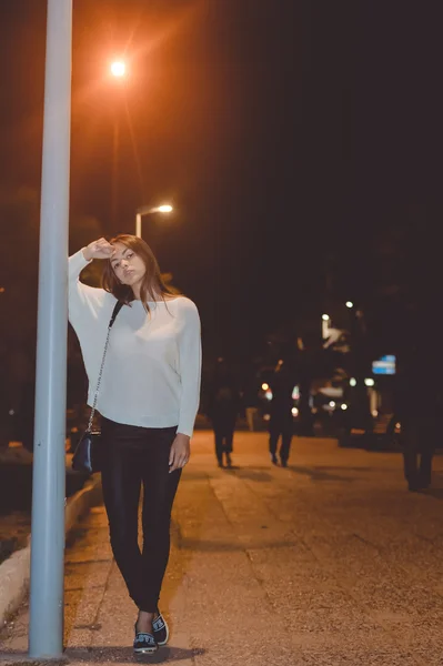 Young brunette female leaning against lamppost on night street background — Stock Fotó