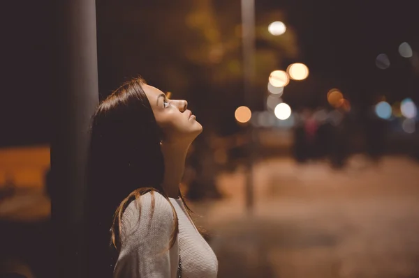 Sad young lady thinking about something leaning against street lamp — Stock Photo, Image