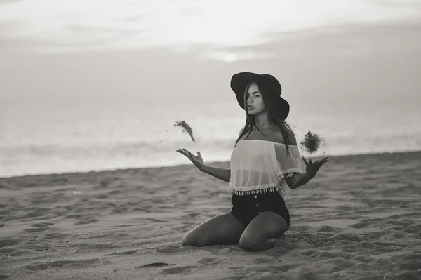 Emocionado morena jogando areia no ar sentado na praia de areia — Fotografia de Stock