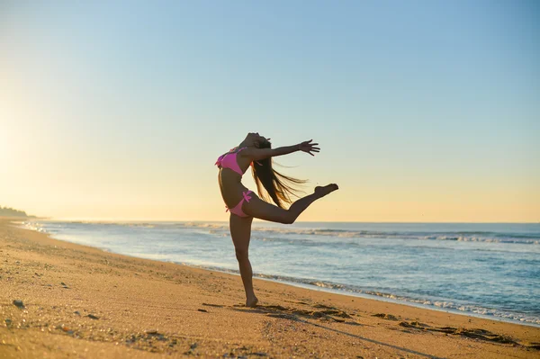 Imagen de una hermosa joven en bikini rosa bailando en la playa. Chica bonita con el pelo largo en el soleado verano al aire libre fondo . — Foto de Stock