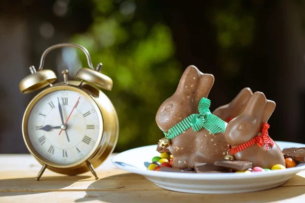 Placa con conejitos de Pascua y dulces de colores al lado del despertador — Foto de Stock