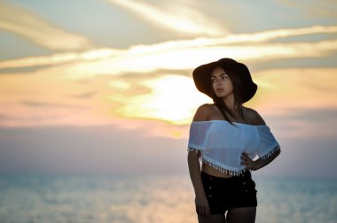 Sensual long haired brunette posing on seashore background at sunset