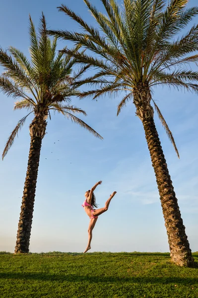 Vacker ung spännande kvinna i bikini hoppa under två palmer. — Stockfoto