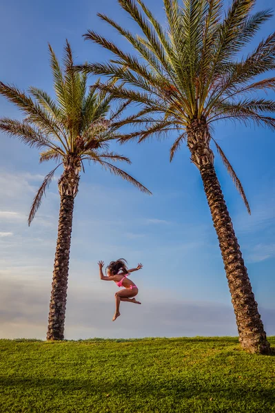 Schöne junge aufregende Frau im Bikini springen unter zwei Palmen. — Stockfoto