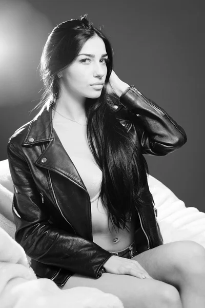 Сексуальная девушка в нижнем белье, кожаная куртка сидит на кровати и смотрит в камеру — стоковое фото