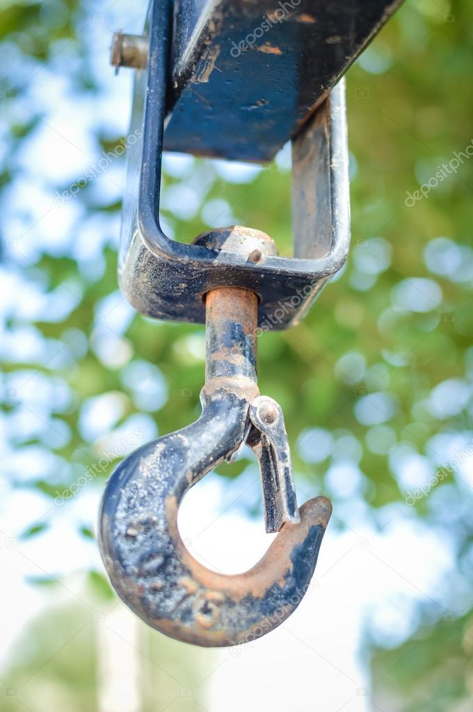 Crane hook hanging over blue sky and green tree in outdoors background