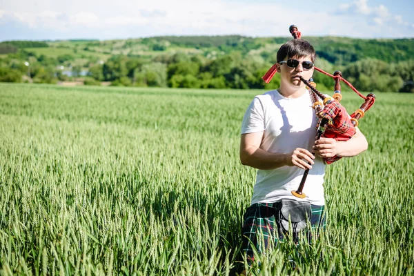 Male in sunglasses enjoying playing pipes in traditional kilt on green outdoors copy space summer field. — Stock Photo, Image