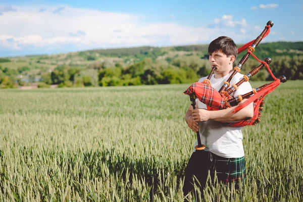 Maschio godendo di giocare tubi in kilt tradizionale su verde all'aperto copiare spazio campo estivo . — Foto Stock