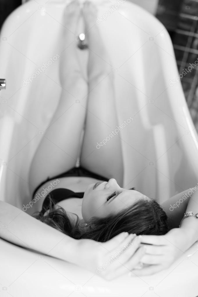 Sexy beautiful young lady having fun relaxing in bath tub. Black and white picture